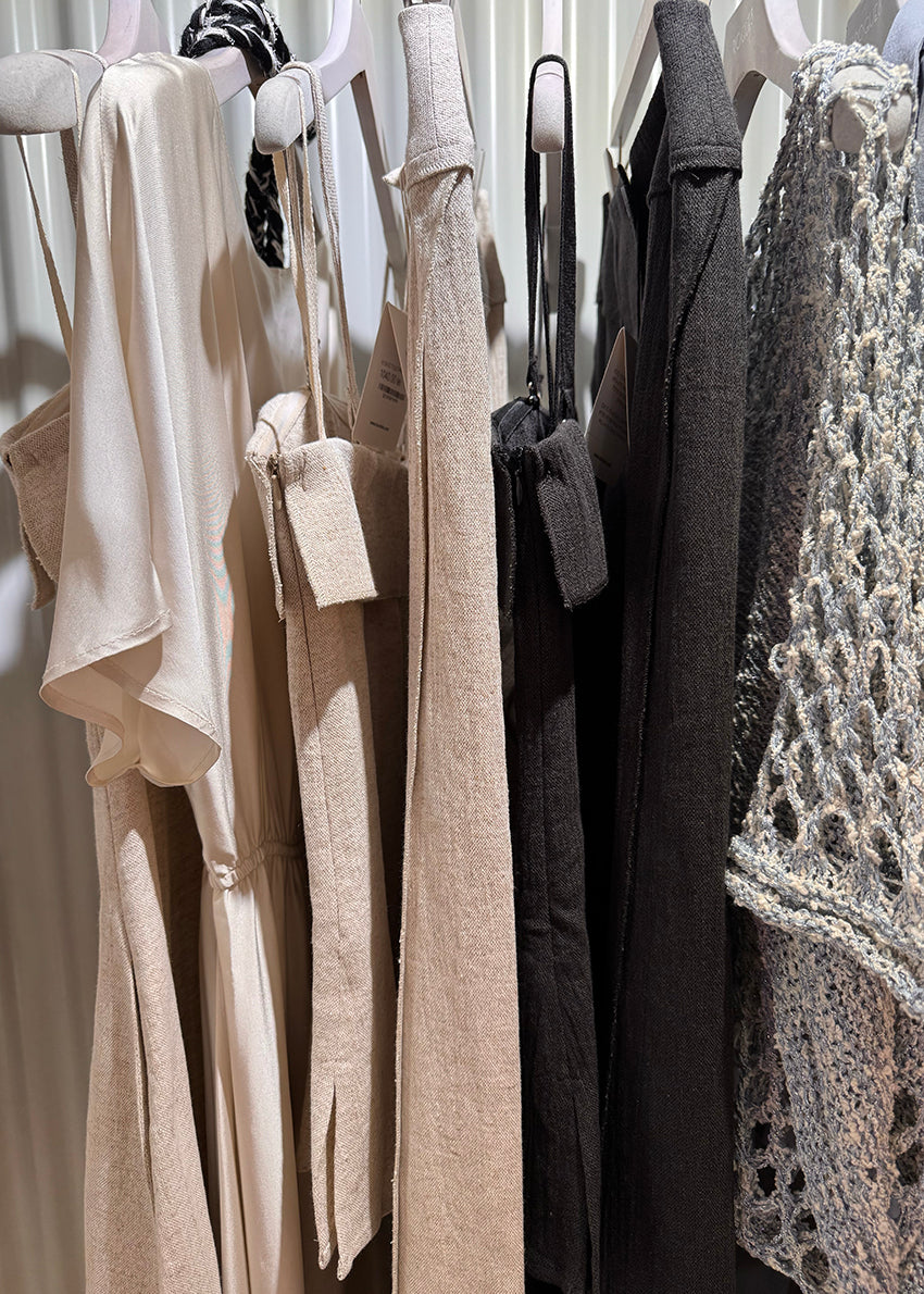 Clothing items hanging on a rack with tags, including shirts and a sweater.