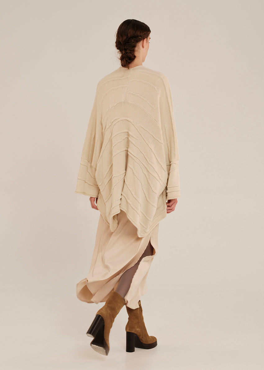Person wearing a beige long cardigan with a plain background