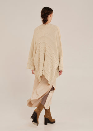 Person wearing a beige long cardigan with a plain background