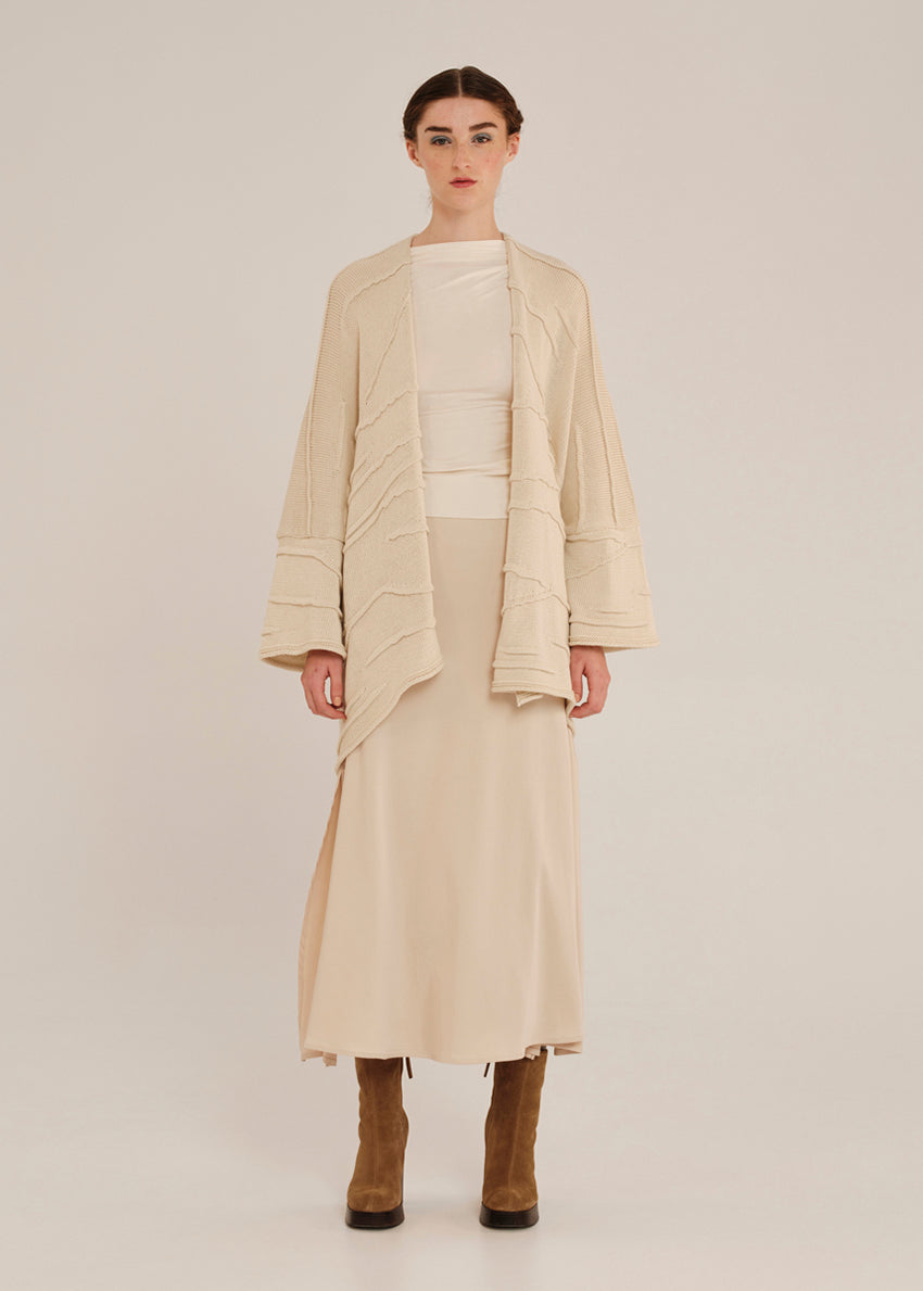 Woman wearing a beige outfit with a long cardigan on a plain background