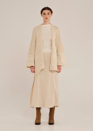 Woman wearing a beige outfit with a long cardigan on a plain background