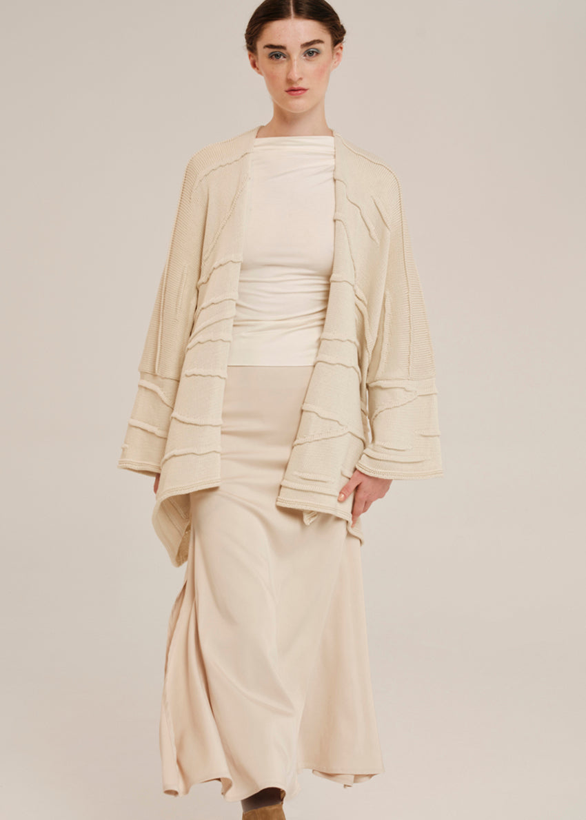 Woman wearing a beige outfit with a matching cardigan on a plain background