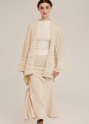 Woman wearing a beige outfit with a matching cardigan on a plain background