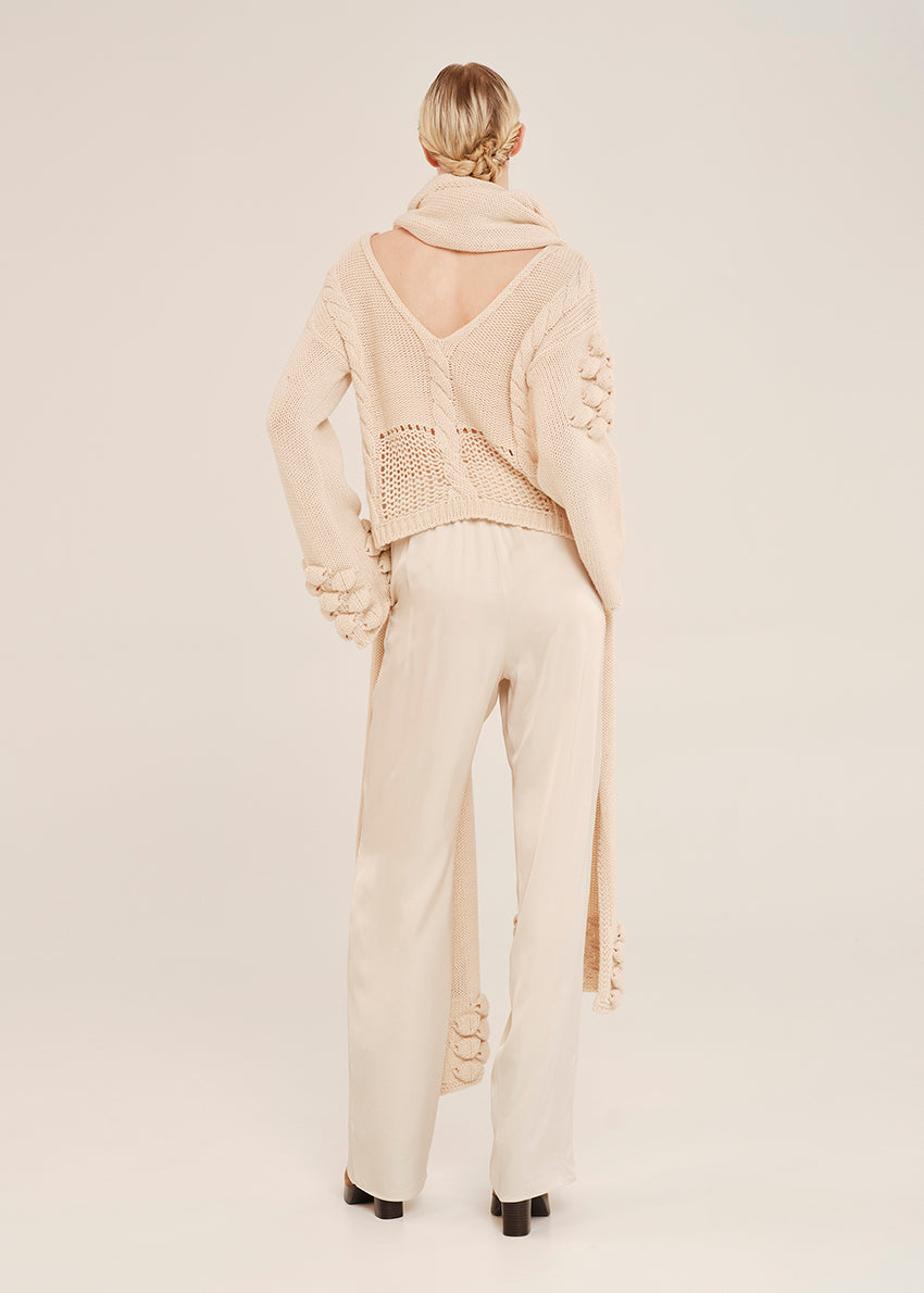 Person wearing a cream-colored knit outfit with a backless top on a plain background