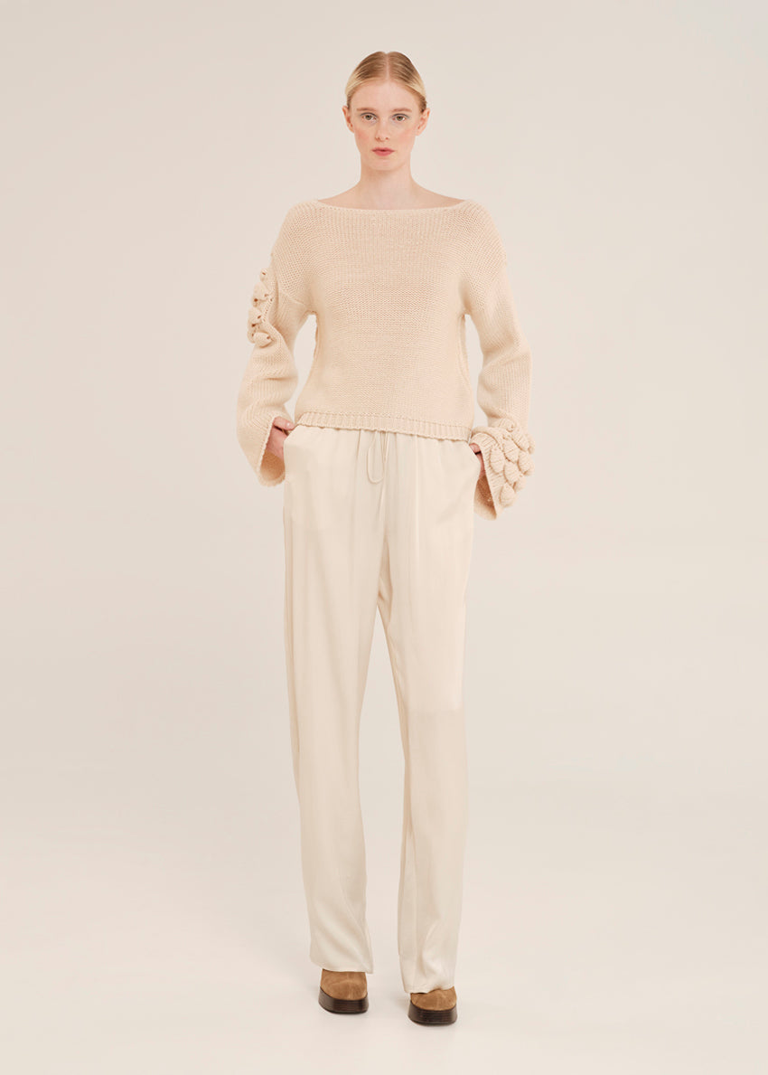 Woman wearing a beige sweater and pants on a light background
