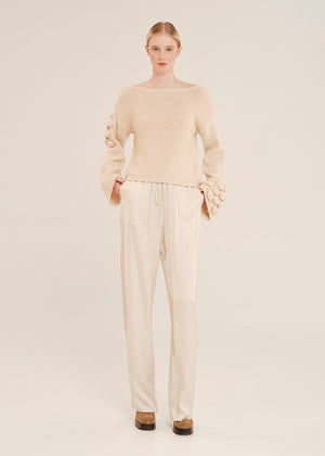 Woman wearing a beige sweater and pants on a light background