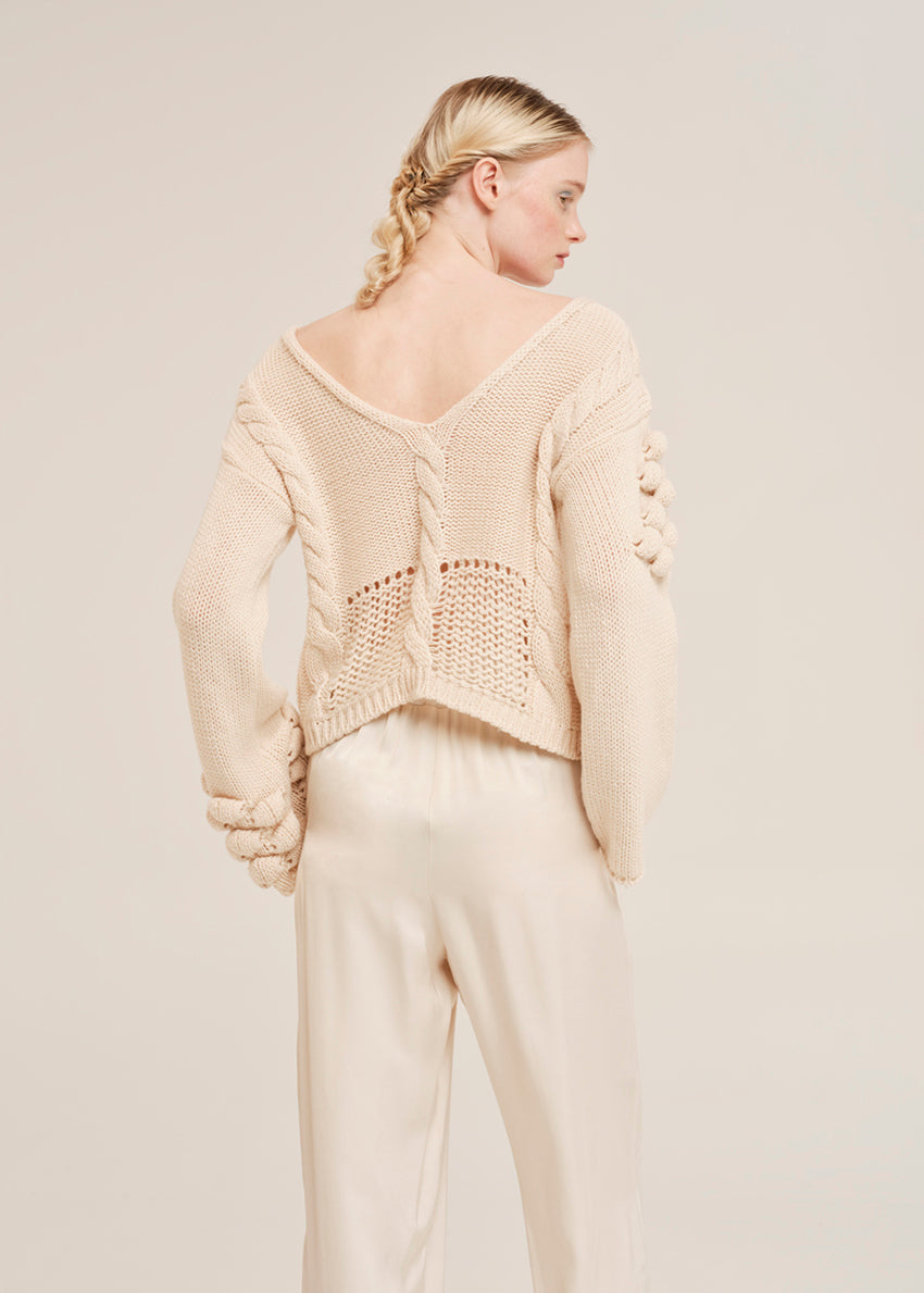 Woman wearing a beige knitted sweater and pants on a plain background