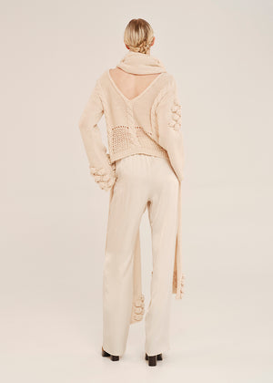 Person wearing a cream-colored knit outfit with a backless top on a plain background