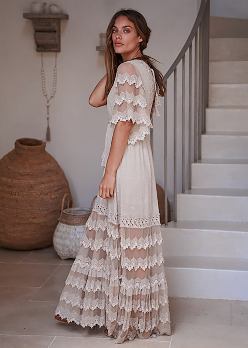 Woman in a lace dress standing in a home setting with a staircase and decorative items.