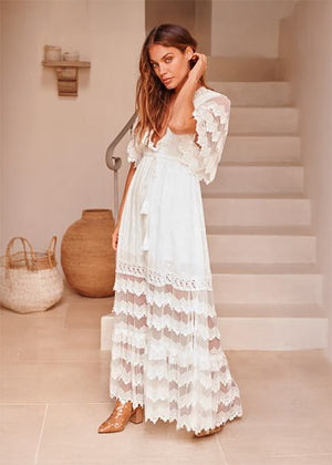 Woman in a white lace dress standing in a home setting with neutral decor.
