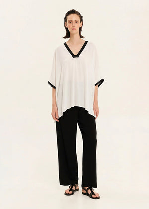 Woman wearing a white blouse with black trim and black pants on a beige background