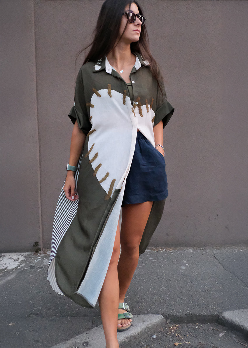 Woman wearing a long, patterned shirt with denim shorts against a plain background