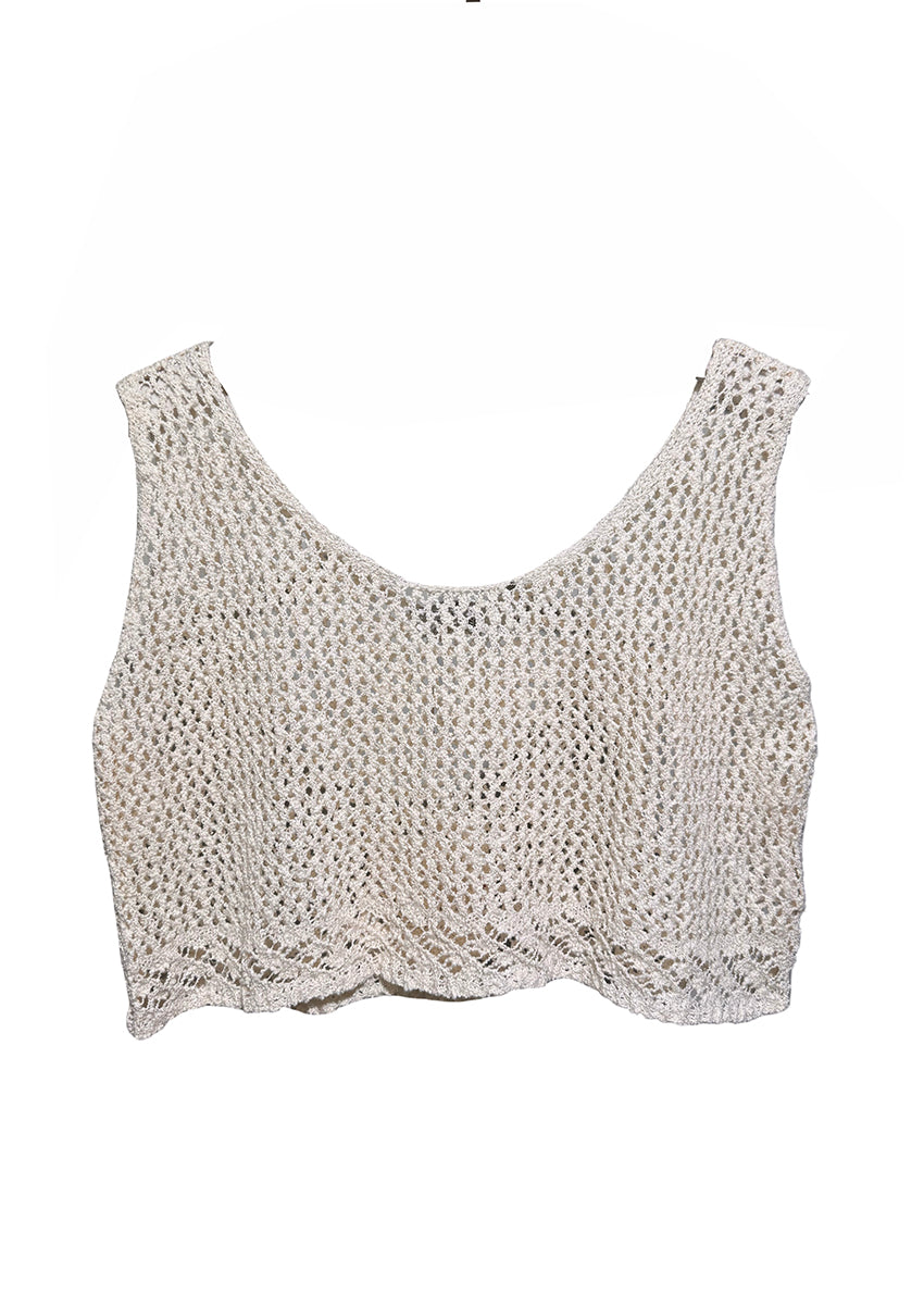 Woman wearing a white crochet top and ripped denim shorts against a dark background