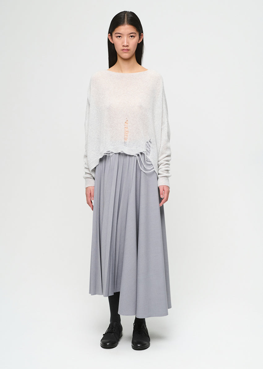 Woman wearing a light gray top and pleated skirt on a white background