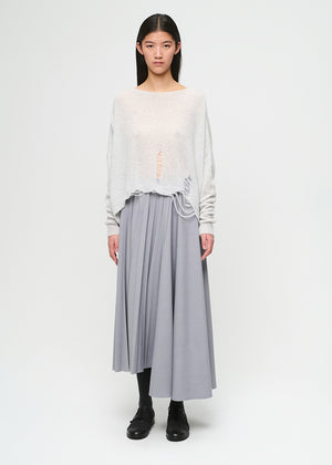 Woman wearing a light gray top and pleated skirt on a white background