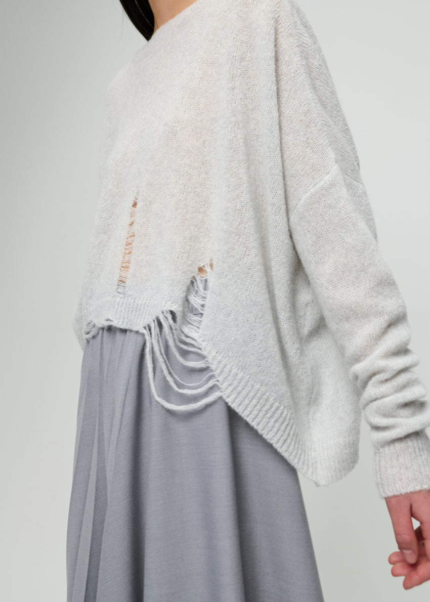 Person wearing a light grey sweater and light grey skirt on a plain background