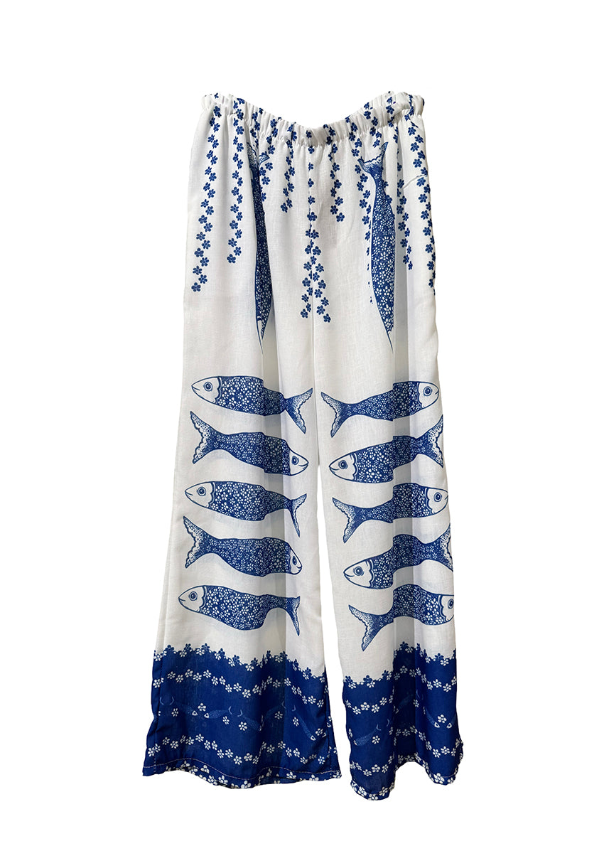 Woman in blue top and fish-patterned pants standing on a beach.
