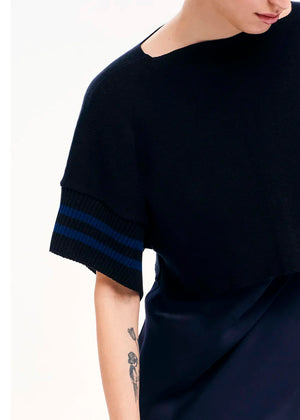 A person viewed from the side wearing a short-sleeved, striped crop top in a dark color.