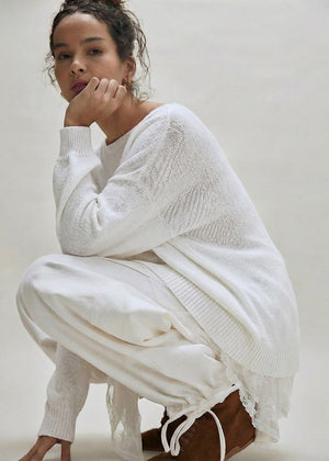 Woman wearing a white knit outfit with brown boots on a plain background