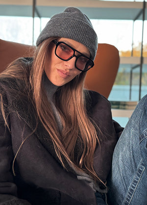 Person wearing a gray beanie and dark coat sitting inside a vehicle.