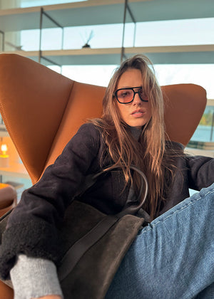 Woman wearing glasses and a dark coat sitting in a modern chair.