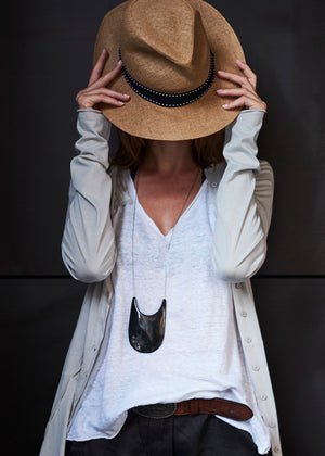 Person wearing a beige hat, light gray cardigan, white shirt, and dark pants against a black background