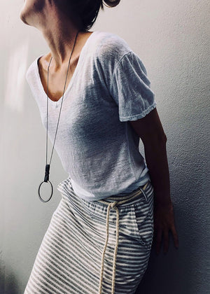 Person wearing a white gray t-shirt and striped skirt against a plain wall.