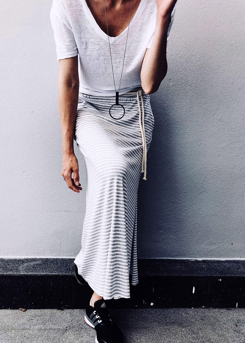 Person wearing a white t-shirt and striped skirt against a gray wall.