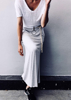 Person wearing a white t-shirt and striped skirt against a gray wall.