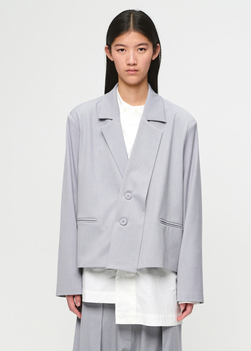 Person wearing a gray blazer over a white outfit on a plain background