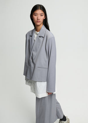 Person wearing a gray blazer over a white outfit on a plain background