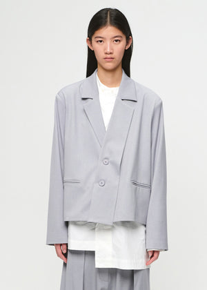 Person wearing a light gray blazer over a white shirt and pants on a plain background