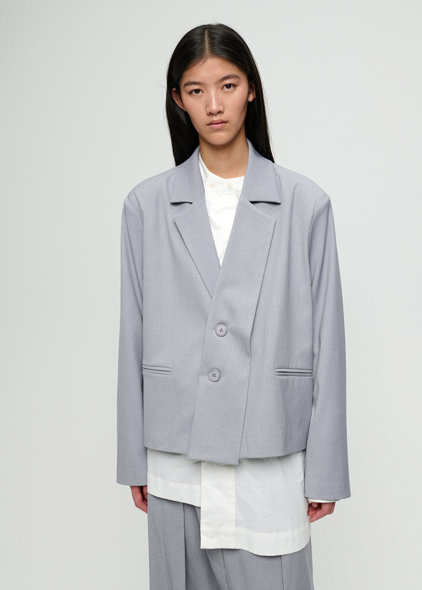 Person wearing a light gray blazer over a white shirt on a plain background