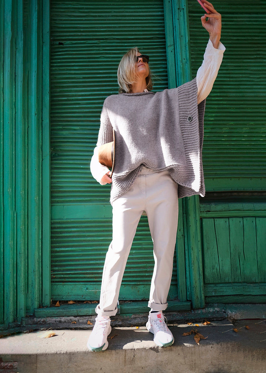 Woman who is taking a selfie wear a grey poncho with white pants