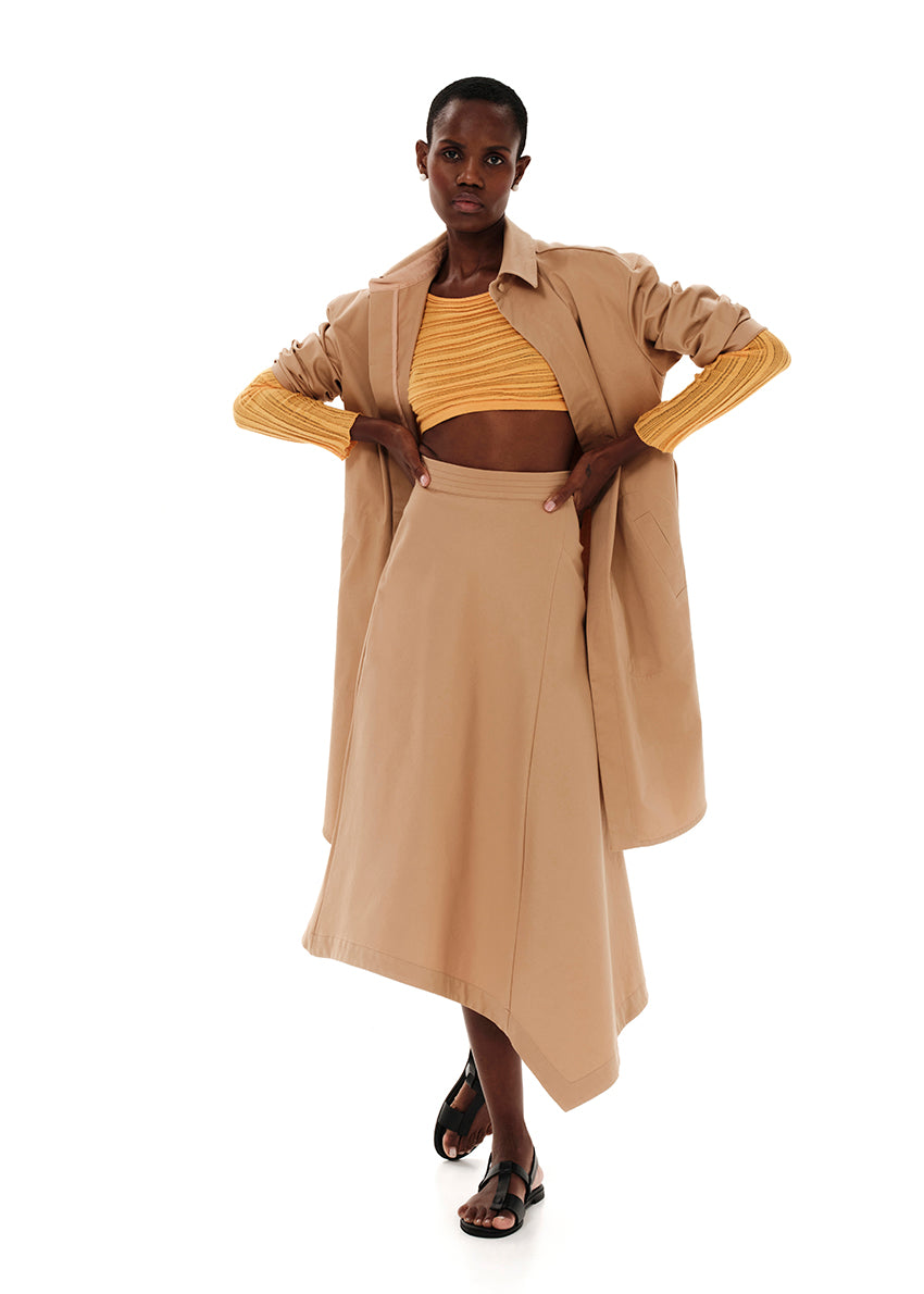 A high-waisted, asymmetrical, beige conical skirt with a zipper closure in the back, worn with platform sandals.