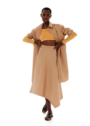 A high-waisted, asymmetrical, beige conical skirt with a zipper closure in the back, worn with platform sandals.