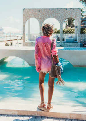 Person standing by a pool with a colorful shirt and sandals, looking at a scenic view.