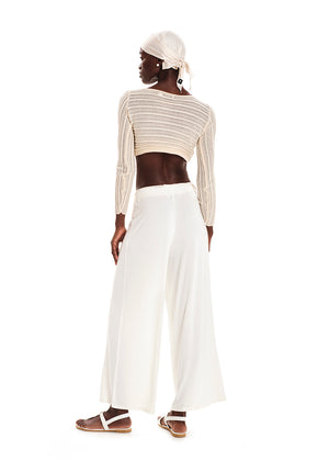 Person wearing a beige knit crop top with white wide pants on a white background 