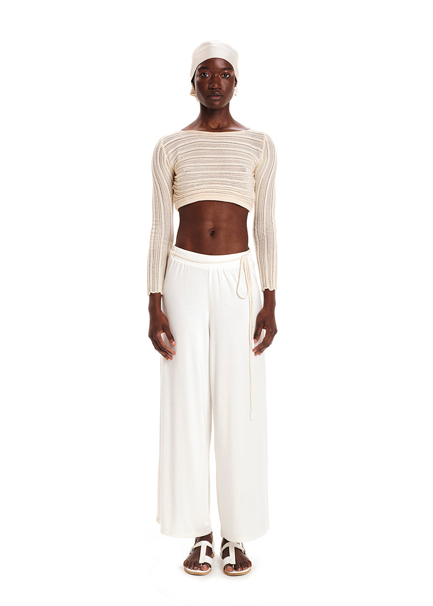 Person wearing a beige knit crop top with white wide pants on a white background 