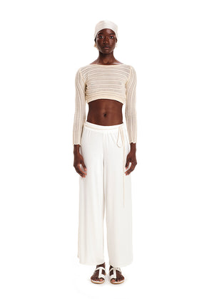 Person wearing a beige knit crop top with white wide pants on a white background 