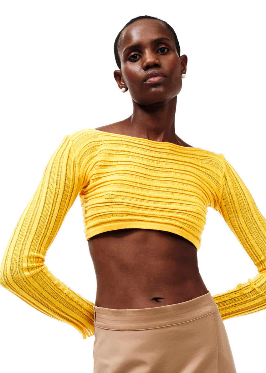A person wearing a yellow long-sleeved crop top with a boat neckline