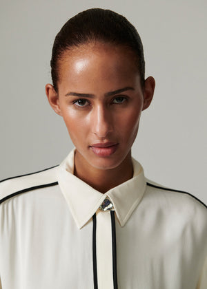 This fluid, button-up top features contrast piping, epaulets at the shoulders, and a dipped hem. There are two pockets at the chest.