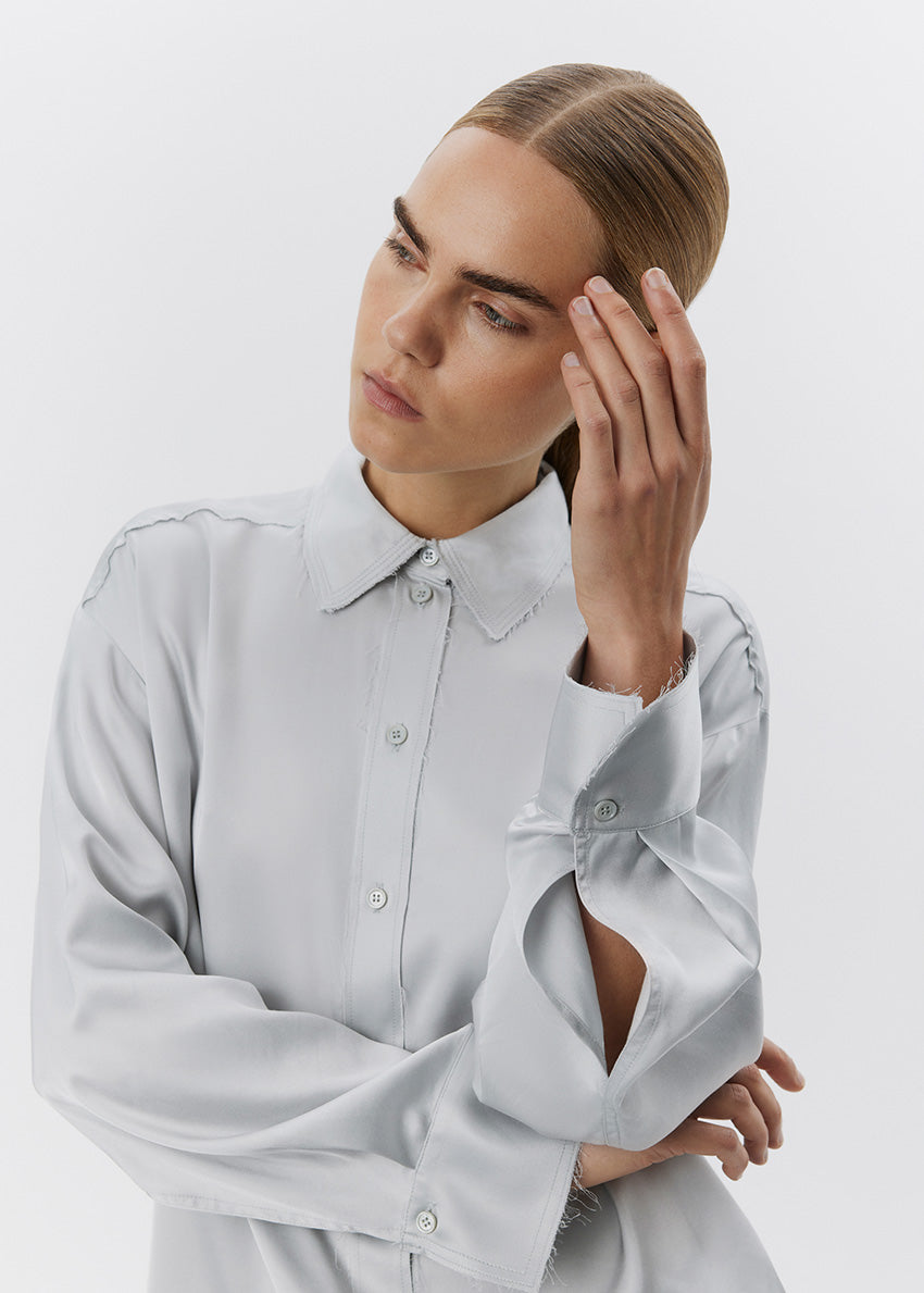 Woman wearing a light gray shirt with a button-up design on a plain background