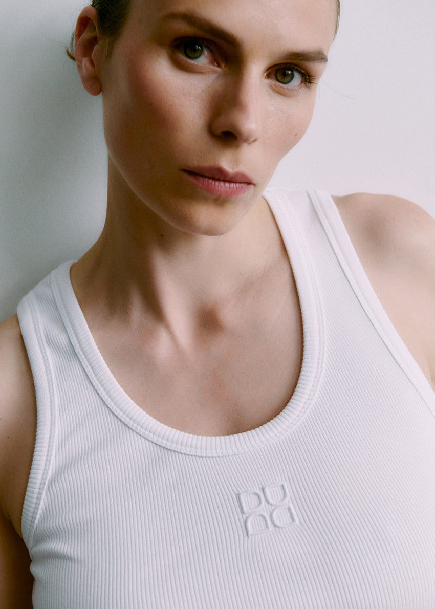 Person wearing a white tank top with a brand logo on a plain background