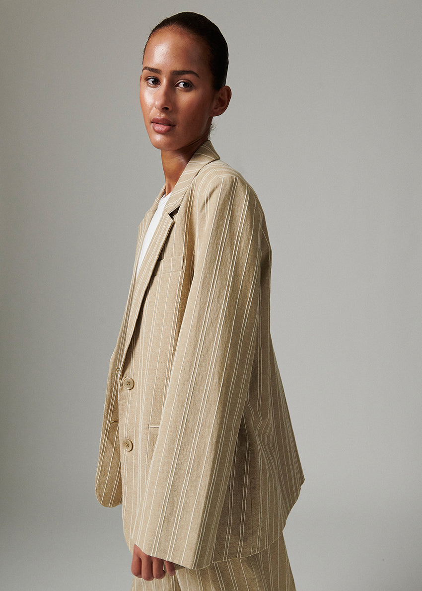 Woman wearing a beige pinstripe suit against a plain background