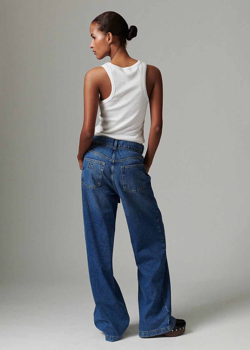 Person wearing a white sleeveless top and blue jeans against a plain background