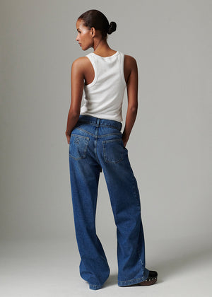 Person wearing a white sleeveless top and blue jeans against a plain background