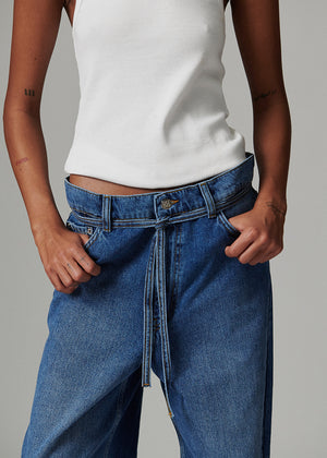 Person wearing a white top and blue jeans with a tie-waist design on a gray background