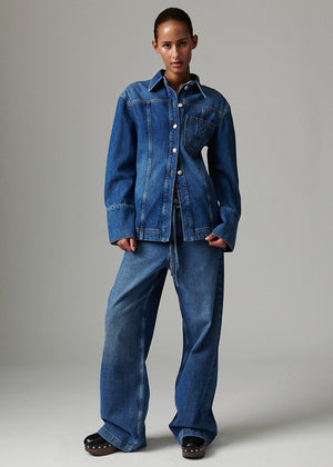 Person wearing a blue denim jacket and jeans on a gray background