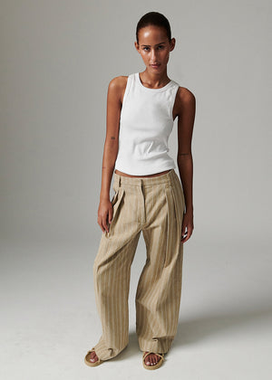 Woman wearing a white sleeveless top and beige pants against a plain background